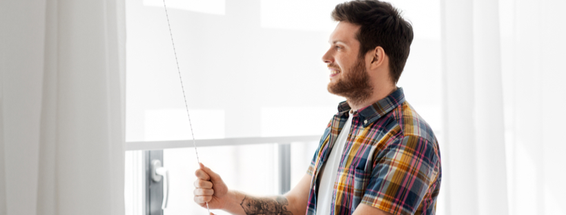 Young man opening window blinds